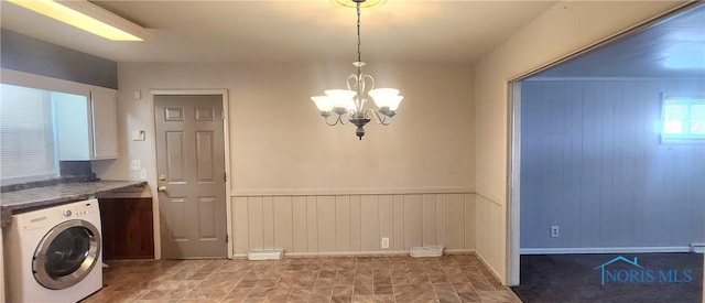 clothes washing area with washer / dryer, wooden walls, and a notable chandelier