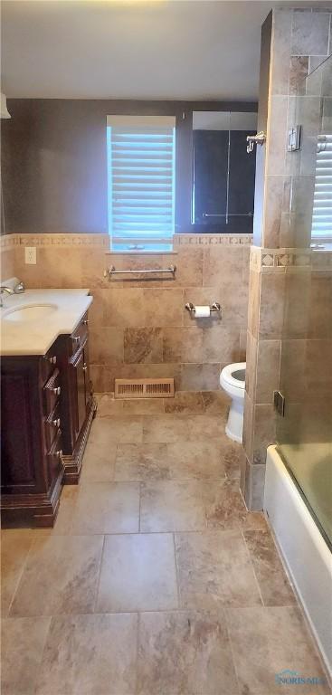 full bathroom featuring shower / bath combination with glass door, vanity, toilet, and tile walls