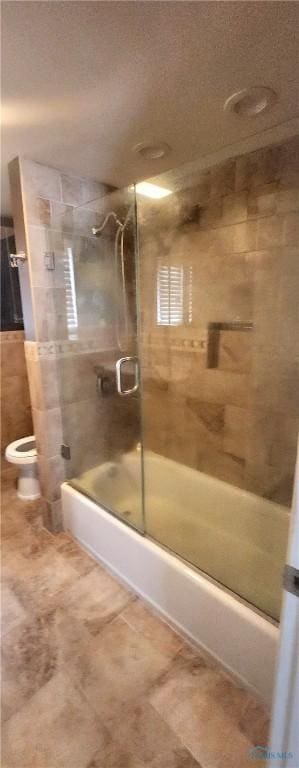 bathroom featuring toilet and combined bath / shower with glass door