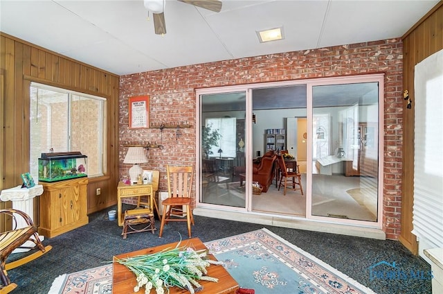 interior space with dark colored carpet, ceiling fan, and brick wall