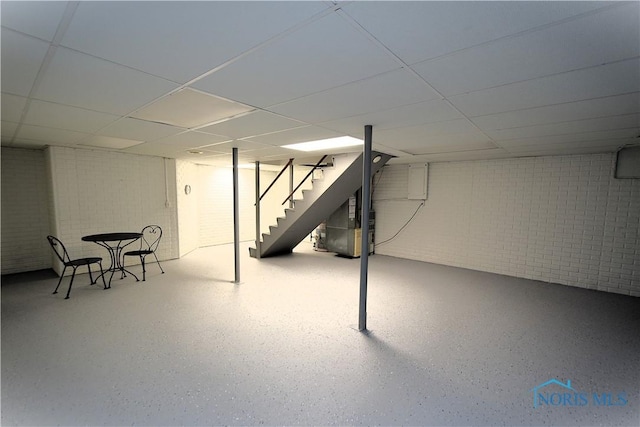 basement featuring a paneled ceiling, brick wall, and heating unit