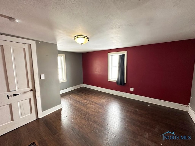 unfurnished bedroom featuring a textured ceiling, multiple windows, and dark wood-type flooring