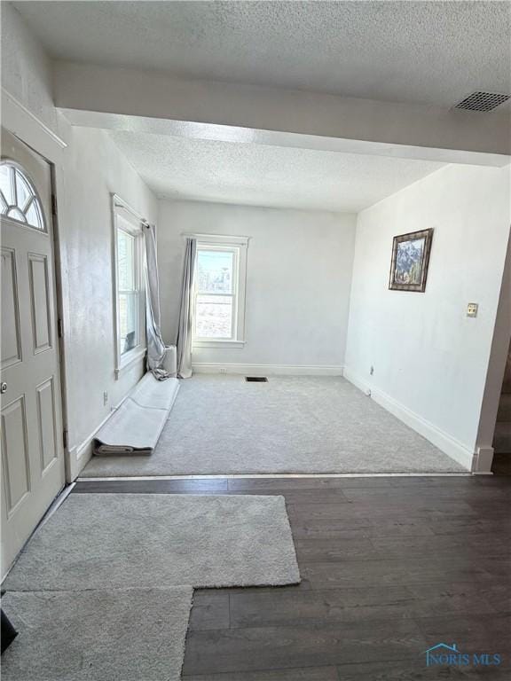 entrance foyer featuring baseboards, visible vents, a textured ceiling, and wood finished floors