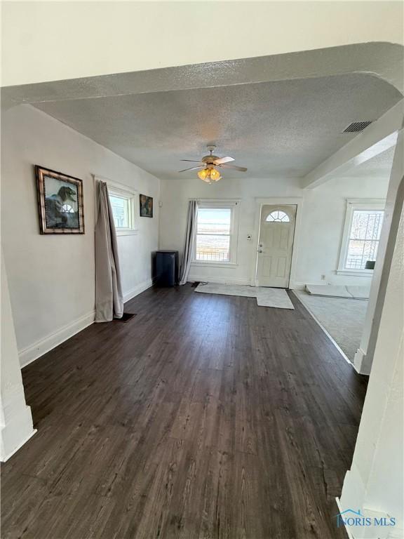 unfurnished living room with dark wood-style floors, a textured ceiling, visible vents, and a healthy amount of sunlight