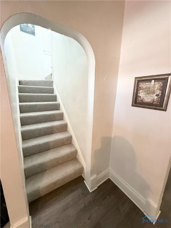 stairs featuring baseboards, arched walkways, and wood finished floors