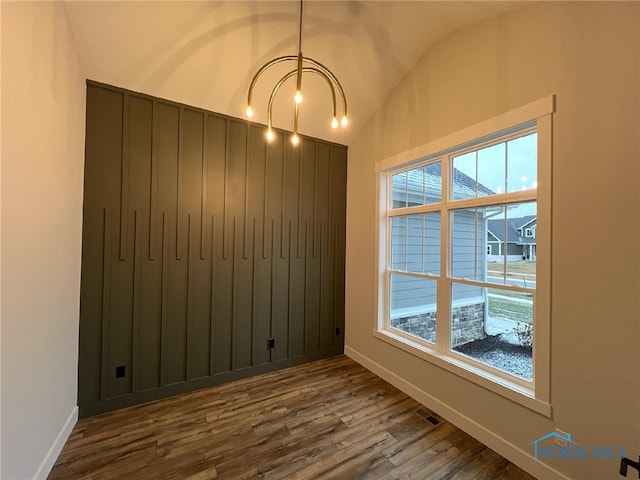 spare room with vaulted ceiling, a wealth of natural light, an inviting chandelier, and wood-type flooring