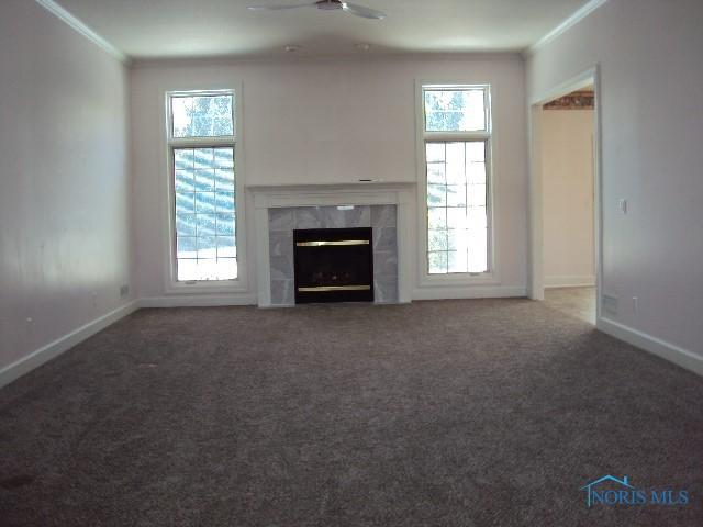 unfurnished living room featuring a high end fireplace, a healthy amount of sunlight, and ornamental molding