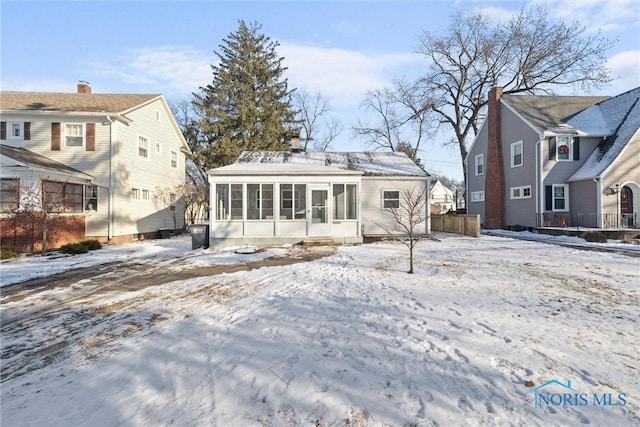 snow covered rear of property featuring a sunroom