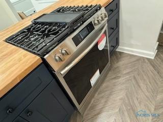 kitchen featuring parquet flooring, stainless steel range with gas cooktop, and butcher block countertops