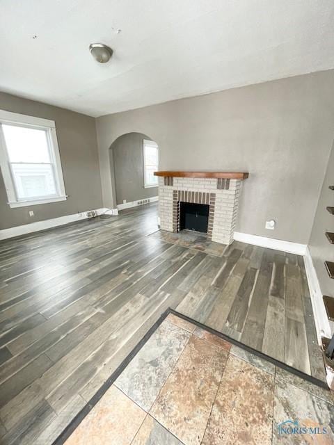 unfurnished living room featuring plenty of natural light, hardwood / wood-style floors, and a brick fireplace