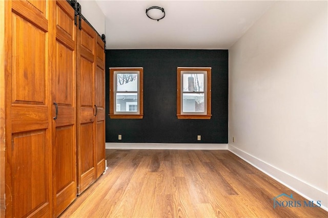 unfurnished bedroom with a barn door and light hardwood / wood-style floors