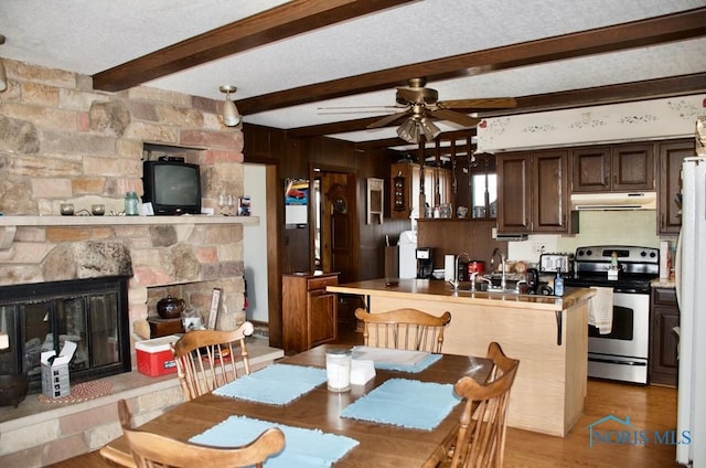 dining space with a textured ceiling, a fireplace, ceiling fan, light hardwood / wood-style floors, and beam ceiling