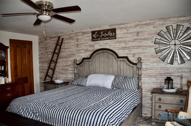 bedroom with a textured ceiling, ceiling fan, and wood walls