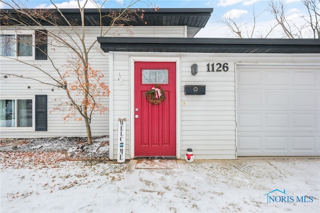 snow covered property entrance featuring a garage