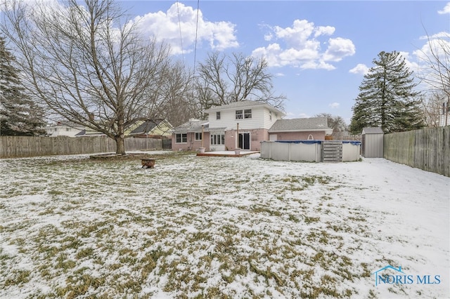 snow covered back of property featuring a shed and a covered pool