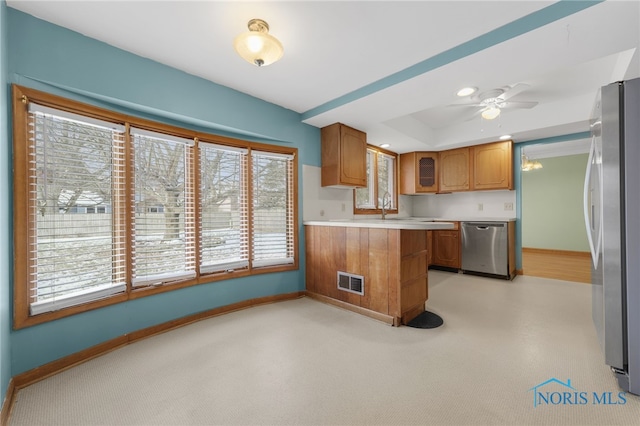 kitchen featuring ceiling fan, kitchen peninsula, a tray ceiling, light carpet, and appliances with stainless steel finishes