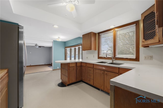 kitchen with stainless steel refrigerator, ceiling fan, sink, a raised ceiling, and kitchen peninsula