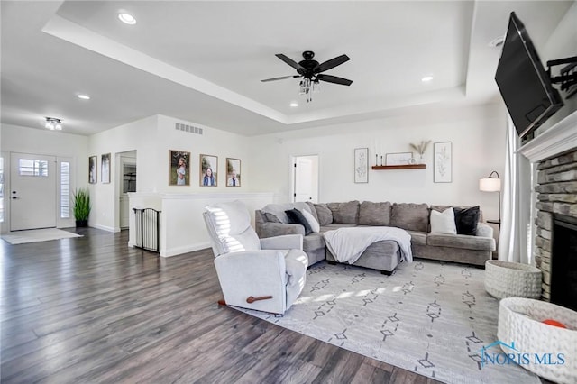 living room with a tray ceiling, a stone fireplace, ceiling fan, and hardwood / wood-style floors