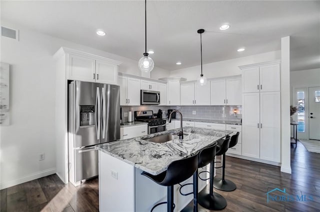 kitchen featuring hanging light fixtures, appliances with stainless steel finishes, white cabinetry, and a kitchen island with sink