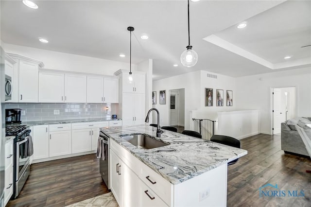 kitchen featuring a center island with sink, white cabinets, sink, light stone countertops, and appliances with stainless steel finishes