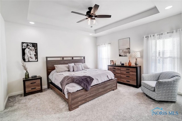 bedroom featuring multiple windows, light colored carpet, a raised ceiling, and ceiling fan