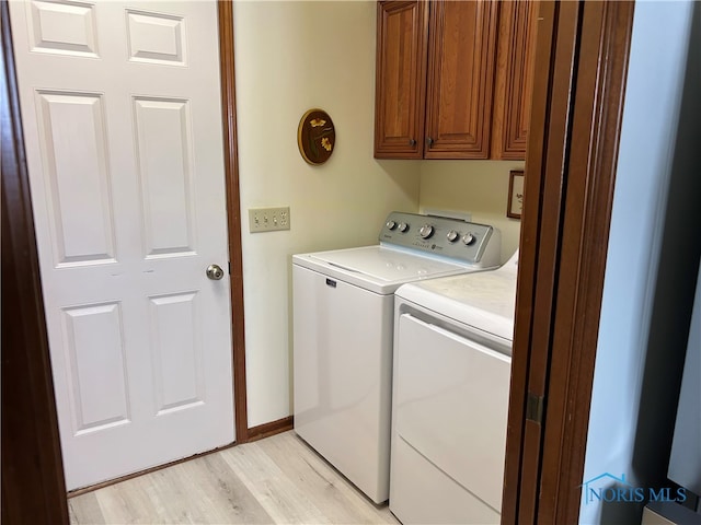 clothes washing area with washing machine and dryer, light hardwood / wood-style flooring, and cabinets