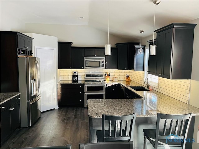 kitchen featuring appliances with stainless steel finishes, tasteful backsplash, vaulted ceiling, pendant lighting, and sink