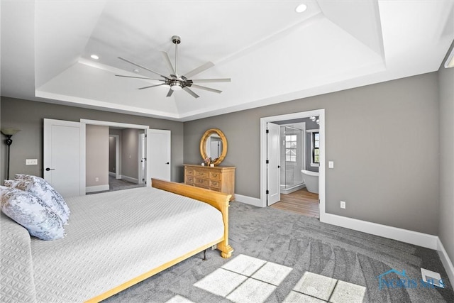 carpeted bedroom featuring ceiling fan, ensuite bath, and a raised ceiling