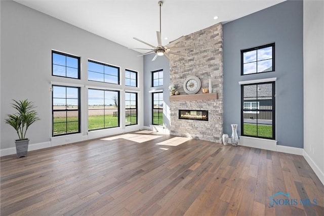 unfurnished living room with a towering ceiling, ceiling fan, hardwood / wood-style flooring, and a stone fireplace