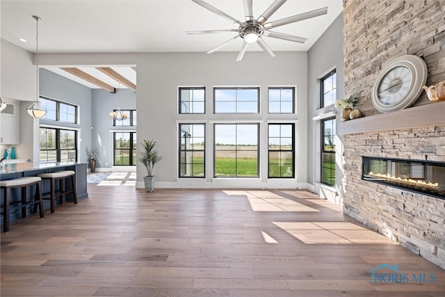 unfurnished living room featuring a wealth of natural light, light hardwood / wood-style floors, beamed ceiling, and a stone fireplace