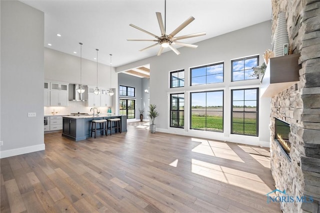 living room featuring a towering ceiling, ceiling fan, a healthy amount of sunlight, and a stone fireplace