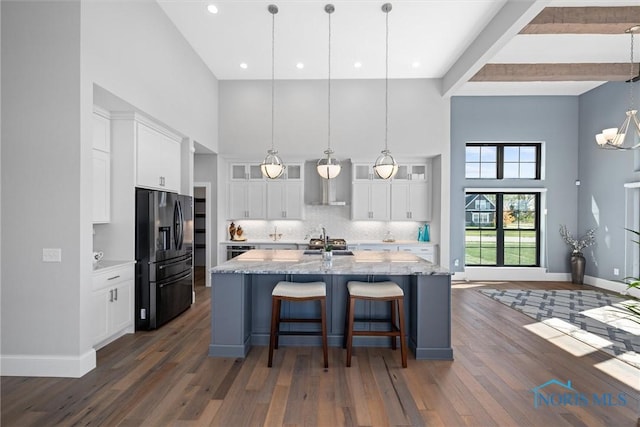 kitchen with black fridge, white cabinets, decorative light fixtures, and an island with sink