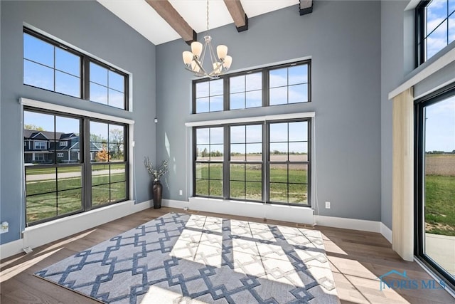 interior space with hardwood / wood-style floors, a notable chandelier, beamed ceiling, and plenty of natural light