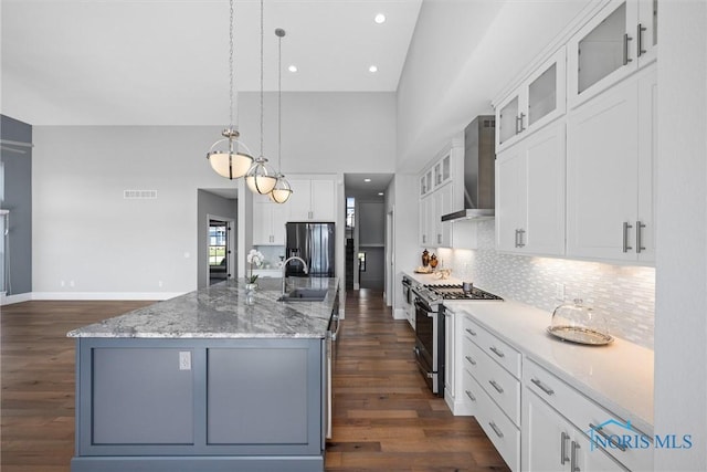 kitchen with appliances with stainless steel finishes, an island with sink, wall chimney exhaust hood, sink, and white cabinetry