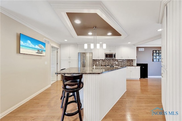 kitchen featuring appliances with stainless steel finishes, dark stone countertops, white cabinets, a center island with sink, and a raised ceiling