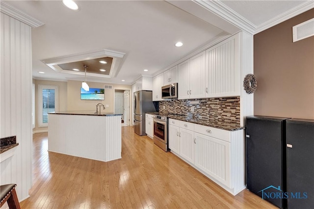 kitchen featuring white cabinetry, appliances with stainless steel finishes, a tray ceiling, pendant lighting, and light hardwood / wood-style floors