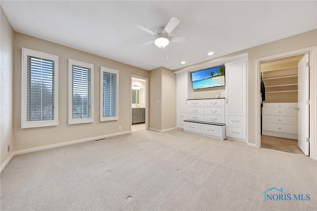 unfurnished bedroom with light carpet, connected bathroom, a spacious closet, and ceiling fan