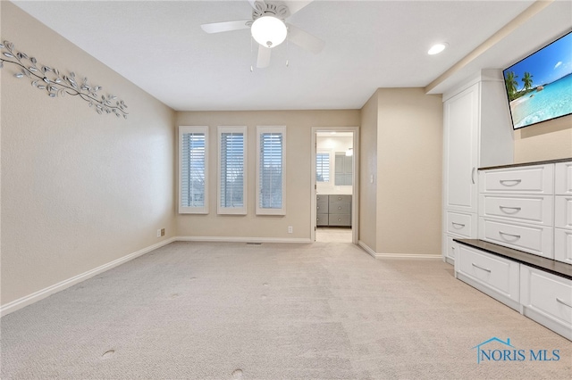 interior space featuring ensuite bathroom, light colored carpet, and ceiling fan