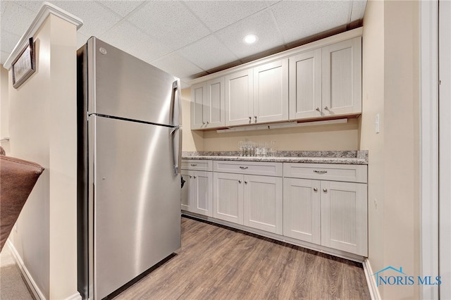 kitchen featuring a paneled ceiling, stainless steel refrigerator, light stone counters, white cabinets, and light wood-type flooring