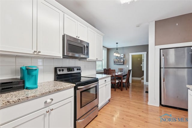 kitchen featuring light hardwood / wood-style floors, stainless steel appliances, white cabinets, decorative light fixtures, and tasteful backsplash