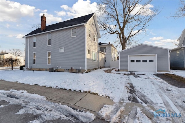 snow covered property featuring central air condition unit, a garage, and an outdoor structure