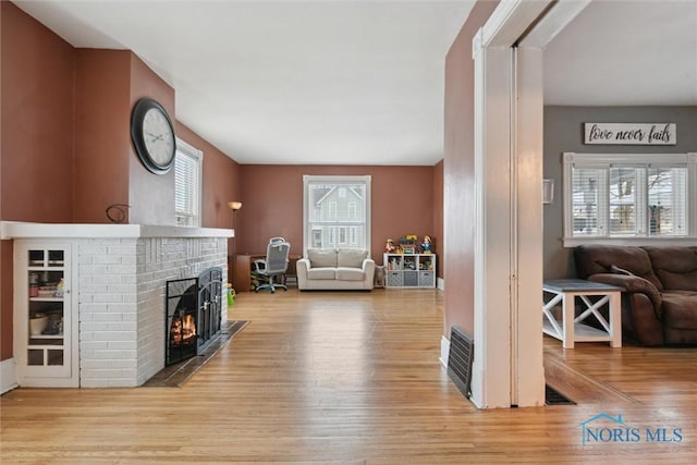 living room featuring light wood-type flooring and a brick fireplace