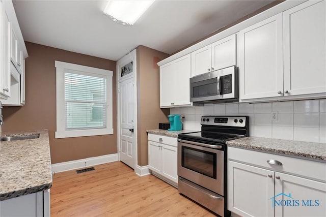 kitchen with light stone counters, tasteful backsplash, white cabinetry, appliances with stainless steel finishes, and sink