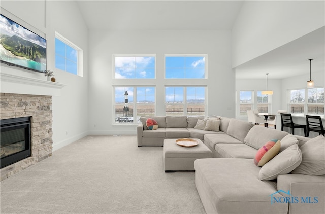 living room featuring light carpet, a high ceiling, and a stone fireplace