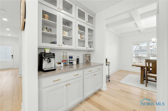 bar with decorative backsplash, white cabinetry, beam ceiling, and coffered ceiling