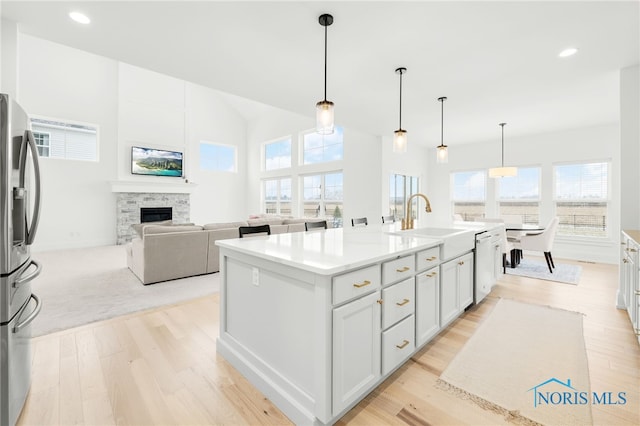 kitchen with stainless steel refrigerator with ice dispenser, a stone fireplace, sink, white dishwasher, and a center island with sink