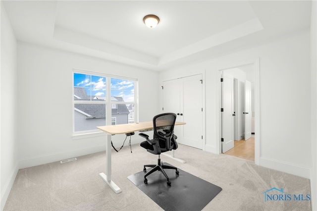 office area featuring a tray ceiling and light carpet