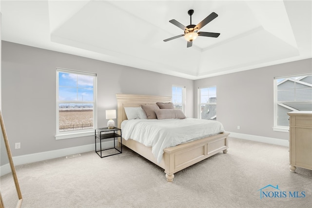 bedroom featuring light carpet, ceiling fan, and a raised ceiling