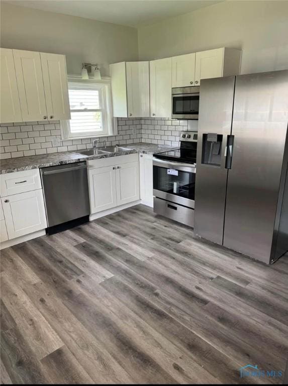 kitchen featuring stainless steel appliances, sink, white cabinetry, stone counters, and wood-type flooring