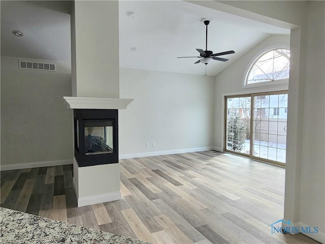 unfurnished living room featuring light wood-type flooring, ceiling fan, a multi sided fireplace, and vaulted ceiling